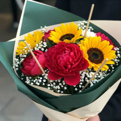 Bouquet of yellow sunflowers and deep pink peonies wrapped in green paper