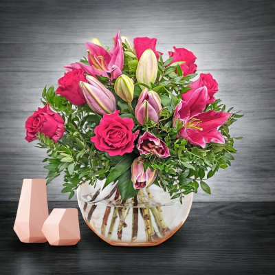 Pink roses and lilies arranged in a clear glass bowl vase
