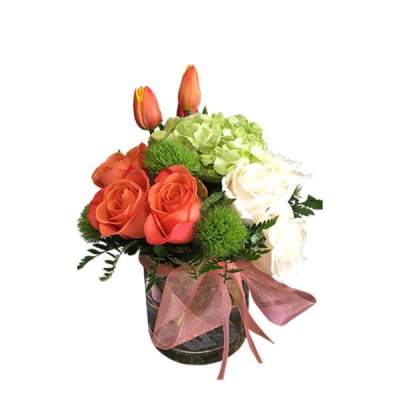 Bouquet of orange roses, white roses, green hydrangea, and tulips in a glass vase