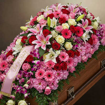 Pink and red floral casket spray with a ribbon on a wooden casket