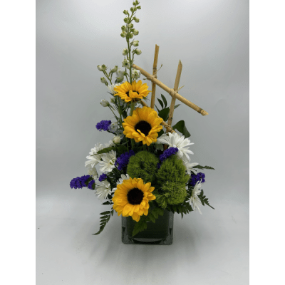 Sunflowers, white daisies, and purple flowers in a square vase with bamboo accents