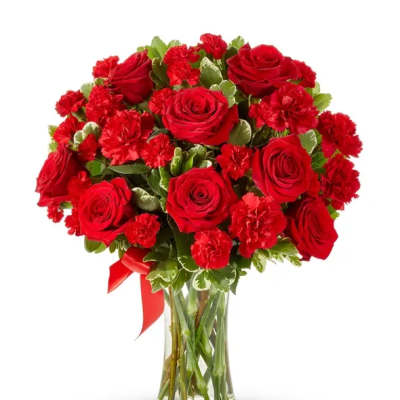 Red roses and carnations in a clear glass vase with a red ribbon