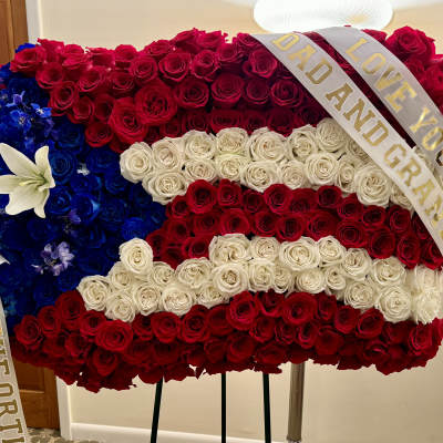 Large rose arrangement in red, white, and blue with a memorial ribbon
