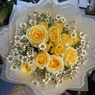 Bouquet of yellow roses and small white daisies wrapped in cream paper