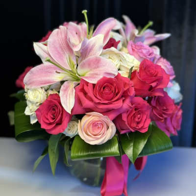 Pink lilies and roses arranged in a glass vase with a ribbon