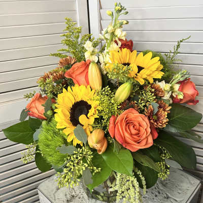 Bouquet of sunflowers, orange roses, and lilies in a glass vase
