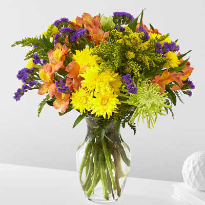 Bright mixed bouquet of yellow, purple, and peach flowers in a glass vase