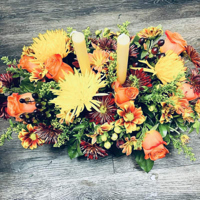 Oval floral centerpiece with orange roses, yellow mums, and two taper candles