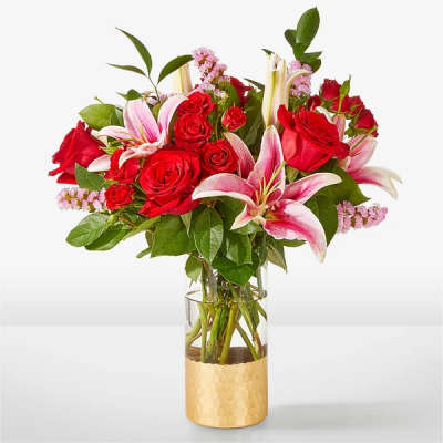 Red roses and pink lilies in a clear vase with a gold base