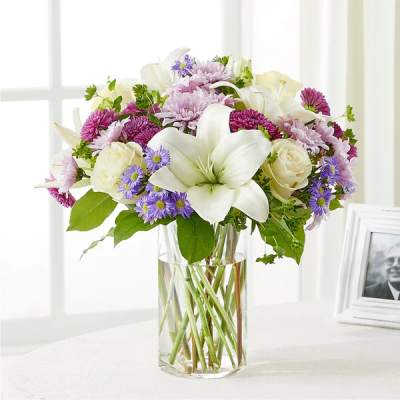 White lilies and purple flowers arranged in a clear glass vase