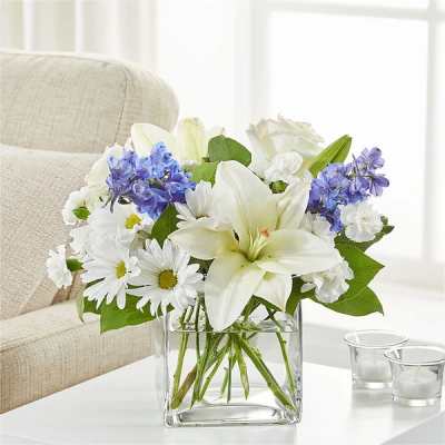 White lilies and daisies with blue flowers in a clear glass vase