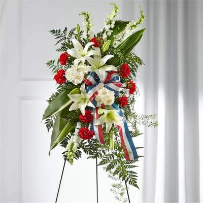 Standing floral spray with white lilies, red carnations, and a patriotic ribbon