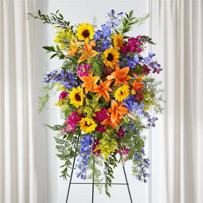 Tall standing spray of sunflowers, lilies, and blue flowers on an easel