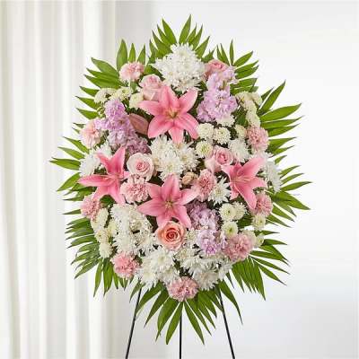 Standing floral wreath with pink lilies, roses, and white blooms on a green leaf frame