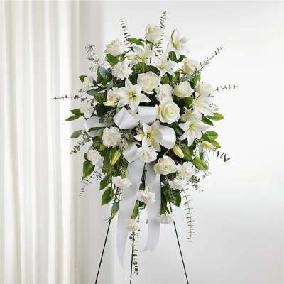 White floral standing spray with lilies, roses, and ribbon on an easel