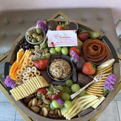 Charcuterie gift tray with fruit, cheese, crackers, nuts, and small purple flowers
