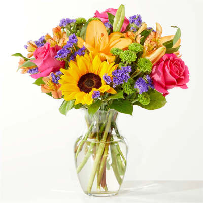 Mixed bouquet of sunflowers, roses, and lilies in a clear glass vase