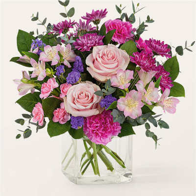 Bouquet of pink roses, carnations, and purple flowers in a clear glass vase