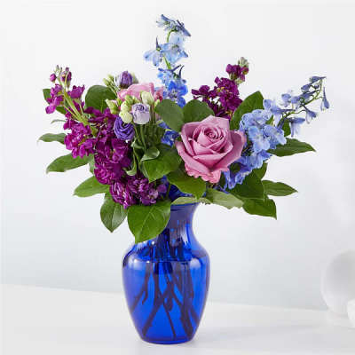 Pink rose bouquet with purple and blue flowers in a blue glass vase