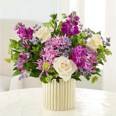 Bouquet of white roses, pink flowers, and purple blooms in a striped gold vase