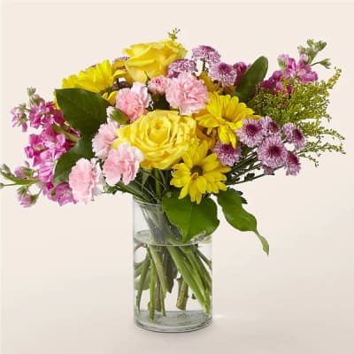 Mixed bouquet of yellow, pink, and purple flowers in a clear glass vase