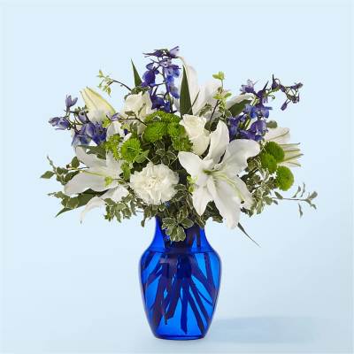 White lilies and purple flowers arranged in a blue glass vase