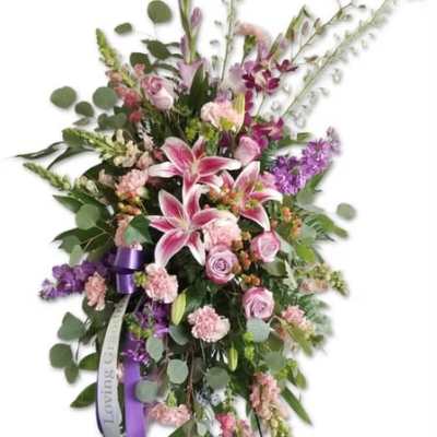 Standing floral spray with pink lilies, roses, and purple accents on an easel