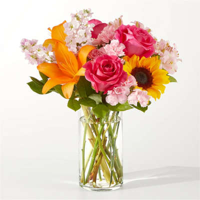 Mixed bouquet of roses, lilies, and a sunflower in a glass vase