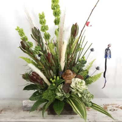 Tall floral arrangement with green blooms and white accents in a wooden container