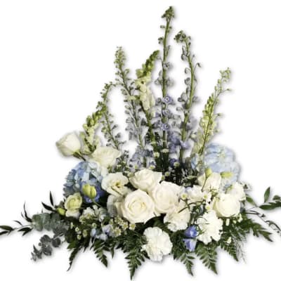 Large white and pale blue floral arrangement with roses, hydrangeas, and tall delphinium spikes