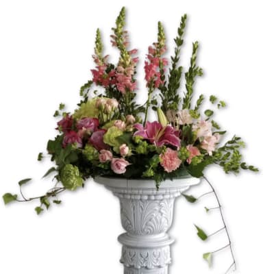 Tall pink and green mixed flower arrangement on an ornate white pedestal column
