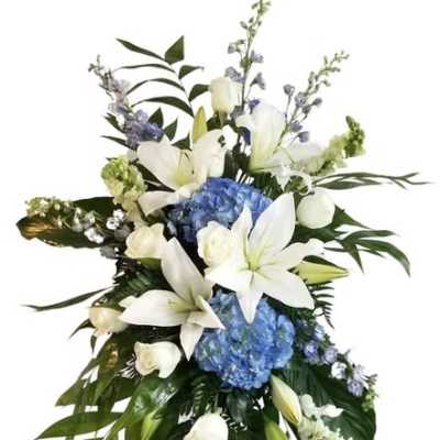 Standing floral spray with white lilies, blue hydrangeas, and an easel