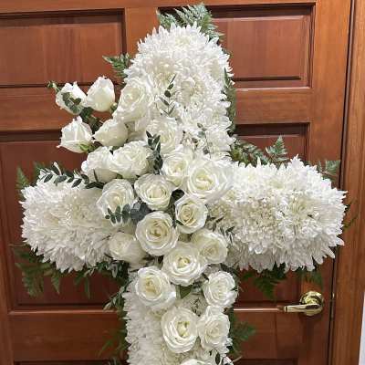 White floral cross on an easel with roses and chrysanthemums