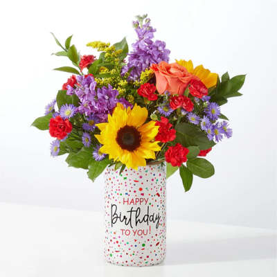 Mixed bouquet in a birthday vase with a sunflower, roses, and purple blooms