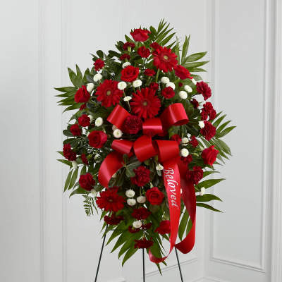Red floral standing spray with a large red ribbon on a black easel