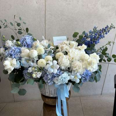 Large blue and white floral arrangement in a white basket with ribbon