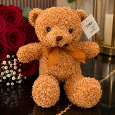 Teddy bear beside red roses and small white flowers