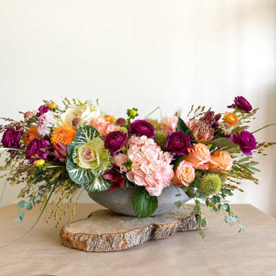 Low floral centerpiece in a gray bowl with pink, orange, and purple blooms