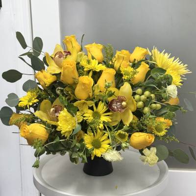 Yellow roses and daisies arranged in a black vase with green foliage.