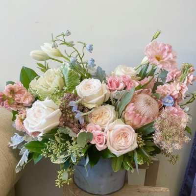 Pastel bouquet of roses, lisianthus, and protea in a gray vase