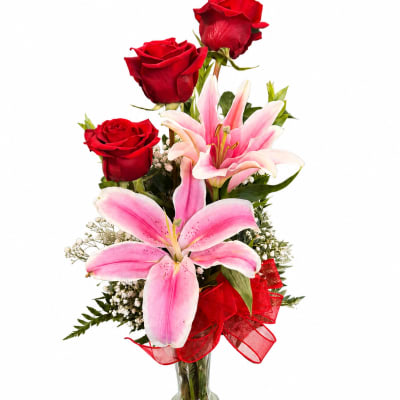 Red roses and pink lilies in a clear glass vase with a red ribbon