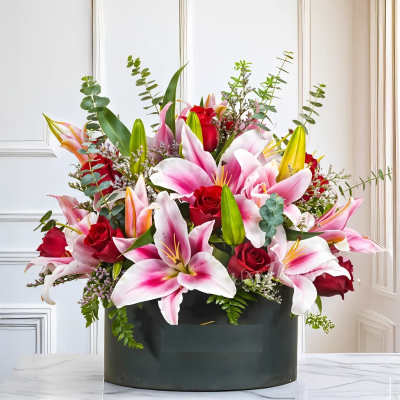 Pink lilies and red roses arranged in a dark box.