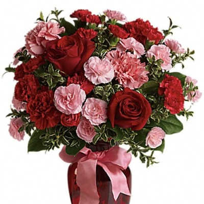 Red roses and pink carnations in a red vase with a pink ribbon