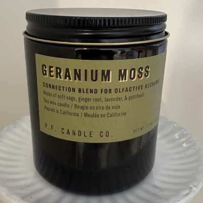 Black jar candle with a tan label on a white pedestal