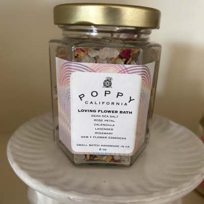 Jar of flower bath salts with a gold lid on a white pedestal