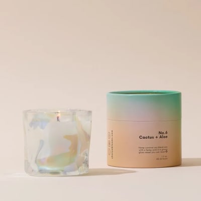 A scented candle in a glass jar beside its pastel cylindrical container