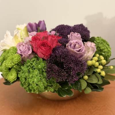Mixed bouquet of roses, hydrangeas, and green blooms in a low bowl vase