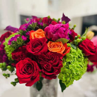 Bouquet of red and orange roses with green hydrangeas in a glass vase