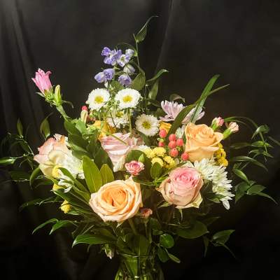 Mixed bouquet of roses, daisies, and purple flowers in a glass vase