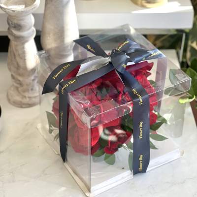 Red roses in a clear gift box tied with a dark ribbon